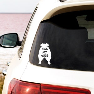 May include: White car with a white vinyl sticker on the back window. The sticker is a silhouette of an Australian Shepherd dog with the text "Kiss My Aussies" on it.