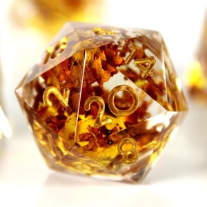 May include: Close-up of five clear, gold-flecked dice with black numbers. The dice are on a white surface.