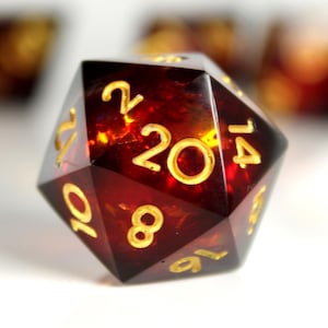 May include: A red twenty-sided die with gold numbers. The die is made of clear plastic with a red tint. The numbers on the die are 2, 4, 6, 8, 10, 12, 14, 16, 18, 20.