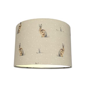 May include: A beige lampshade with a white polka dot pattern and a repeating image of brown rabbits.