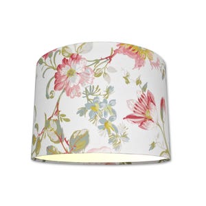 May include: A cylindrical lampshade with a floral pattern. The design features pink and red flowers, green leaves, and blue accents on a white background. The lampshade is lit from within, casting a warm glow.