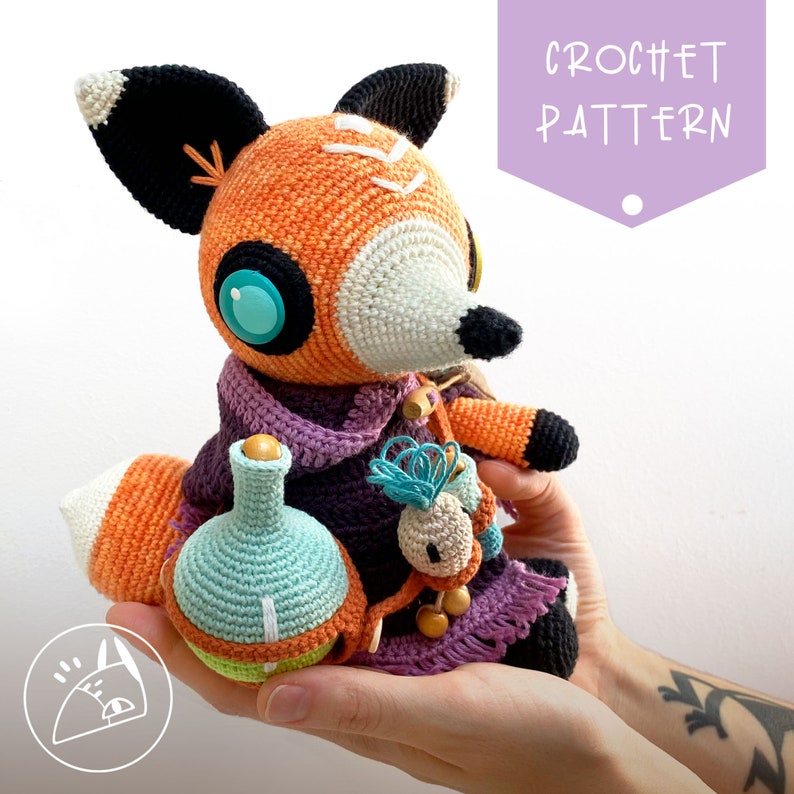 Peut inclure: Patron de crochet pour un jouet amigurumi de renard. Le renard est orange et blanc avec des yeux bleus et tient une petite bouteille et une fleur. Le renard porte une &eacute;charpe violette.