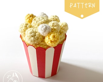 May include: A crocheted popcorn bucket with yellow and white popcorn pieces. The bucket is red and white striped.