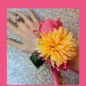 This is a beautiful corsage with yellow, hot pink and green artificial flowers and matching silver tone adjustable iridescent ring.