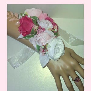 This is a beautiful corsage with pink and white artificial flowers. Matching silver tone adjustable pink bling gem ring.