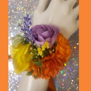 This is a corsage with orange, lavender, yellow artificial flowers. Faux yellow and purple greenery accents embedded. Matching yellow ring.