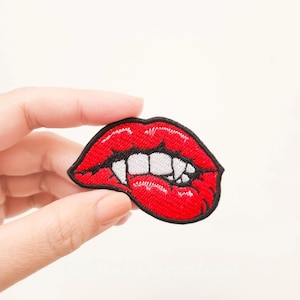 Könnte beinhalten: Roter gestickter Patch mit einem Paar Lippen, die Zähne zeigen. Die Lippen sind mit schwarzem Faden umrandet.