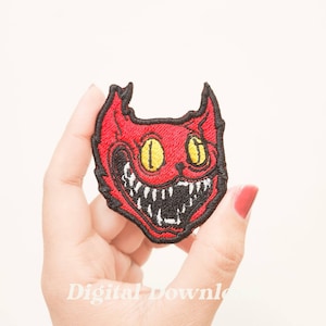 May include: Red embroidered iron-on patch of a cat with a wide, toothy grin and yellow eyes.
