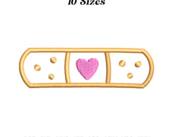 Puede incluir: Un diseño bordado en dorado de un vendaje con un corazón rosa en el centro. El diseño está disponible en 10 tamaños y en los siguientes formatos: DST, EXP, HUS, JEF, PES, SEW, VP3, XXX.