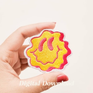 May include: A yellow smiley face patch with a pink outline and white stitching. The patch is in the shape of a distorted circle.