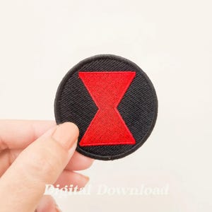 Puede incluir: Un parche bordado negro y rojo con el símbolo de Black Widow. El símbolo es una forma de reloj de arena roja sobre un fondo circular negro.