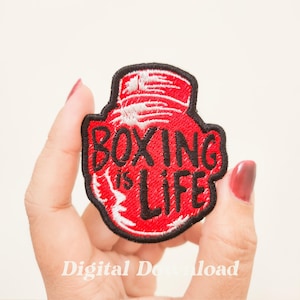 May include: Embroidered patch featuring a red boxing glove design with the words "BOXING is LIFE" in white lettering. The patch has a black border and is held against a light background.