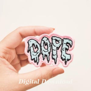 Pode incluir: Um remendo de ferro bordado rosa e azul com a palavra "DOPE" em letras pingando.