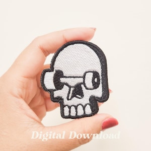 May include: White embroidered skull patch with a black dumbbell for an eye. The patch is held in a hand.