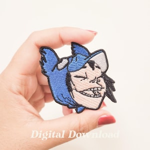 May include: An embroidered iron-on patch featuring a cartoon character wearing a blue and gray hat. The character has a mischievous expression and is wearing a blue hooded jacket.