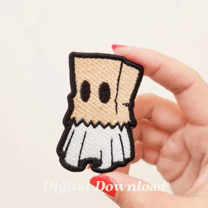 May include: Embroidered iron-on patch of a person wearing a brown paper bag over their head with two black eye holes. The person is wearing a white skirt and has black shoes.