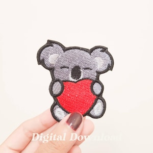 Può includere: Toppa ricamata raffigurante un koala grigio che tiene un cuore rosso. Il koala ha gli occhi chiusi e dettagli neri. La toppa ha un bordo nero e il testo "Digital Download" è visibile.