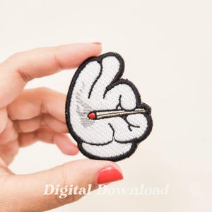 May include: White embroidered patch depicting a hand holding a lit cigarette. The hand is in a peace sign gesture. The patch is ideal for adding a touch of personality to clothing, bags, or other accessories.