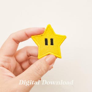 Pode incluir: Um remendo amarelo em forma de estrela com olhos pretos. O remendo é bordado e tem uma superfície ligeiramente texturizada.