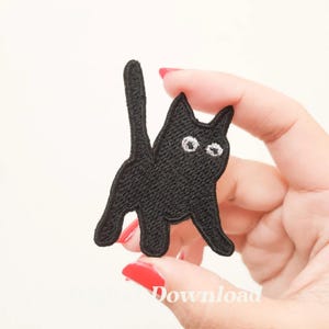 May include: Black embroidered iron-on patch of a cat with white eyes. The cat is standing on all fours with its tail raised in the air.