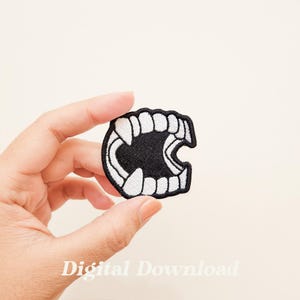 May include: A black and white embroidered patch of a set of fangs. The fangs are white and the inside of the mouth is black.