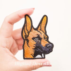 May include: Embroidered patch featuring a German Shepherd dog's head in shades of brown, black, and tan. The patch has a black border and is likely designed to be ironed on or sewn onto fabric. The dog's eye is detailed.