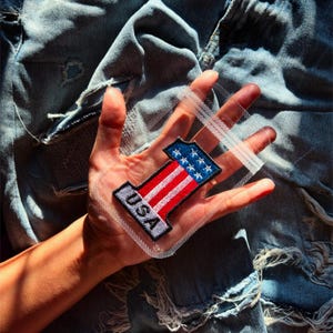 May include: A red, white, and blue embroidered patch shaped like the number one with the word "USA" below it. The patch is in a clear plastic bag.