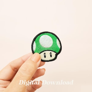 Könnte beinhalten: Ein gestickter Pilz-Patch in Grün und Weiß mit schwarzem Umriss. Der Pilz hat einen weißen Punkt oben und zwei schwarze Augen.