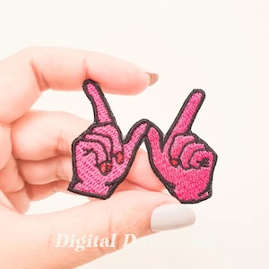 May include: Pink embroidered iron-on patch of two hands forming the letter "W" with black stitching.