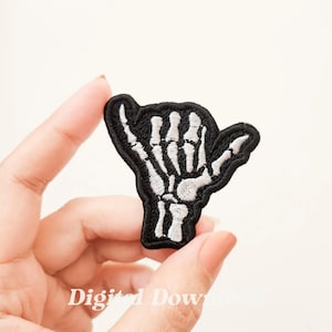 Könnte beinhalten: Schwarzer gestickter Bügel-Patch mit einer Skeletthand, die das Shaka-Zeichen zeigt. Der Patch ist weiß und schwarz.