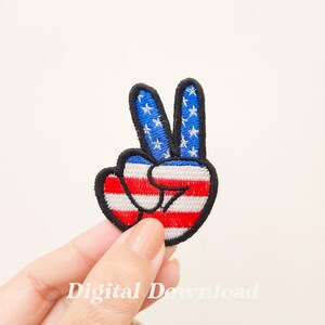 May include: A peace sign hand with the American flag design. The hand is red, white, and blue with white stars on the blue part of the hand.