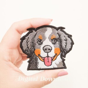 Może przedstawiać: Haftowana naszywka przedstawiająca uśmiechniętego Berneńskiego Psa Pasterskiego. Naszywka ma czarny kontur, szare futro, białe oznaczenia i pomarańczowe policzki. Język psa jest różowy. Tekst "Digital Download" jest widoczny na dole.