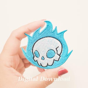 May include: A white skull with blue eyes is set on fire with blue flames. The skull and flames are embroidered on a patch.