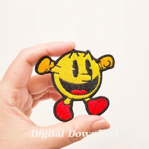 以下が含まれることがあります： 大きな笑顔、黒い目、赤い足を持つ、象徴的な黄色のキャラクターが特徴の刺繍されたパックマンパッチ。パッチは黄色の腕と黒いアウトラインを持っています。「Digital Download」というテキストが下部に表示されます。