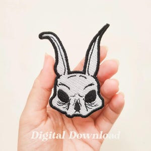 Könnte beinhalten: Ein weiß gestickter Bügel-Patch mit einem Kaninchen-Schädel mit schwarzen Augen und Ohren.