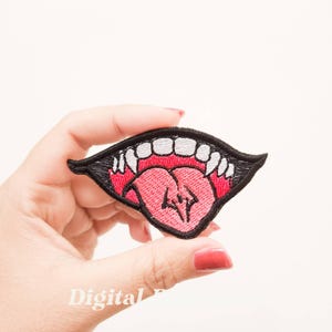 May include: Embroidered iron-on patch featuring a black mouth with white teeth and a pink tongue sticking out.
