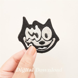 May include: Black and white embroidered iron-on patch of a cartoon cat with a mischievous grin. The cat has one eye closed and the other eye wide open.
