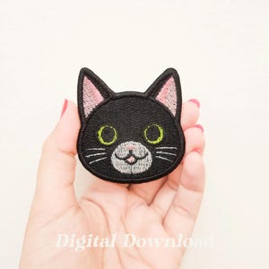 May include: Black embroidered cat face patch with pink ears, green eyes, and a white nose and mouth.