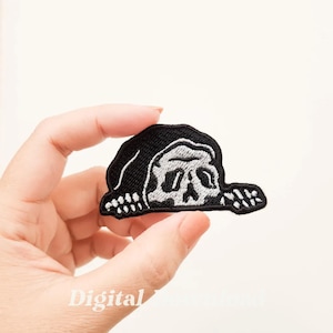 May include: Black and white embroidered iron-on patch featuring a skull with a black hooded cloak peeking out from behind it.