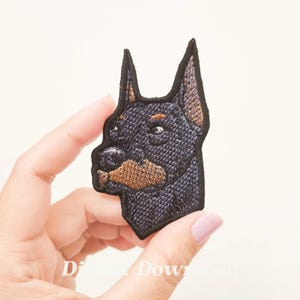 Könnte beinhalten: Gestickter Aufnäher mit dem Kopf eines schwarzen und braunen Dobermann Pinschers.