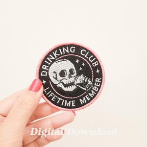 May include: Black and white embroidered patch with a pink outline. The patch features a skull drinking from a can with the text "Drinking Club Lifetime Member" around the skull.