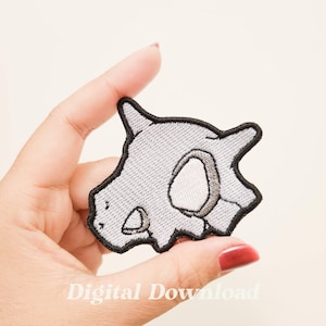 May include: Embroidered patch featuring a gray skull with a black outline. The patch has a textured appearance and a white oval shape in the center. The text "Digital Download" is visible at the bottom.