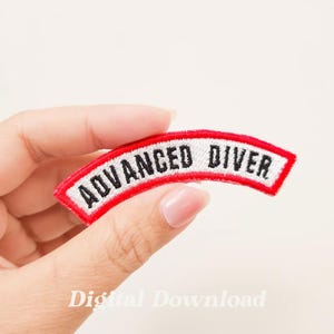 Może przedstawiać: Biała naszywka haftowana z czerwonym obramowaniem, w kształcie łuku. Naszywka zawiera napis "ADVANCED DIVER" czarnymi literami.
