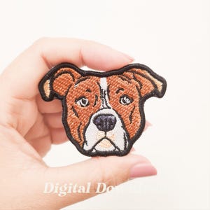 Puede incluir: Parche bordado con la cara de un perro. El parche tiene un esquema de color marrón y blanco con contornos negros. La cara del perro está detallada con características bordadas, incluyendo ojos, nariz y orejas. El parche está diseñado para planchar o coser sobre tela.