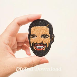 Puede incluir: Parche bordado para planchar con un retrato de dibujos animados sonriente de Drake. El parche es negro con tonos de piel marrones y labios rojos.