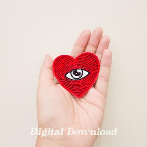 Peut inclure: Patch brodé en forme de cœur rouge avec un œil blanc au centre. L'œil a une pupille noire et un iris brun.