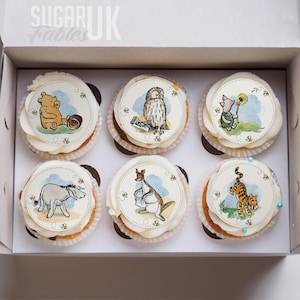 A box containing six cupcakes decorated with illustrations of Winnie the Pooh and other characters from the Winnie the Pooh series.