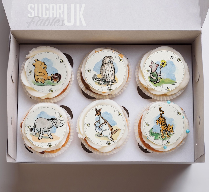 A box containing six cupcakes decorated with illustrations of Winnie the Pooh and other characters from the Winnie the Pooh series.