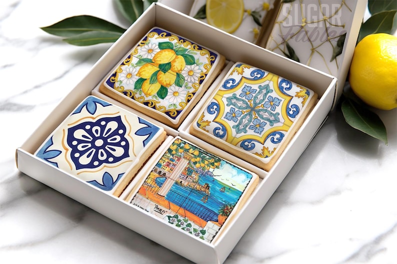A white box containing four decorative cookies with various patterns and designs, including a floral pattern, a geometric pattern, and a landscape scene.