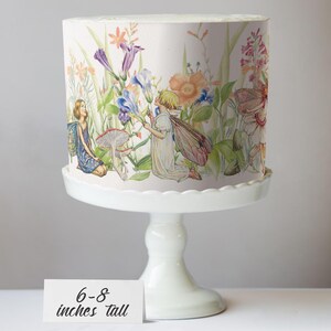 A cake stand with a decorative paper featuring illustrations of fairies and flowers on it.